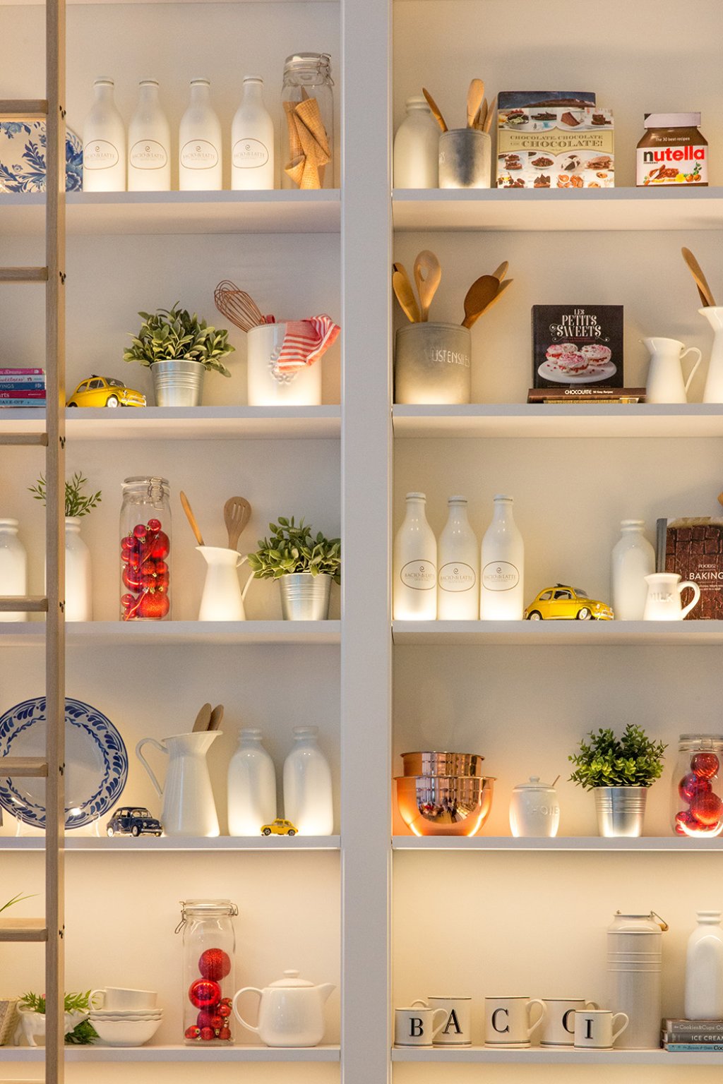 A photograph of a set of neatly arranged kitchen shelves displaying packages of food, bottles, utinsils, plates and small model cars.