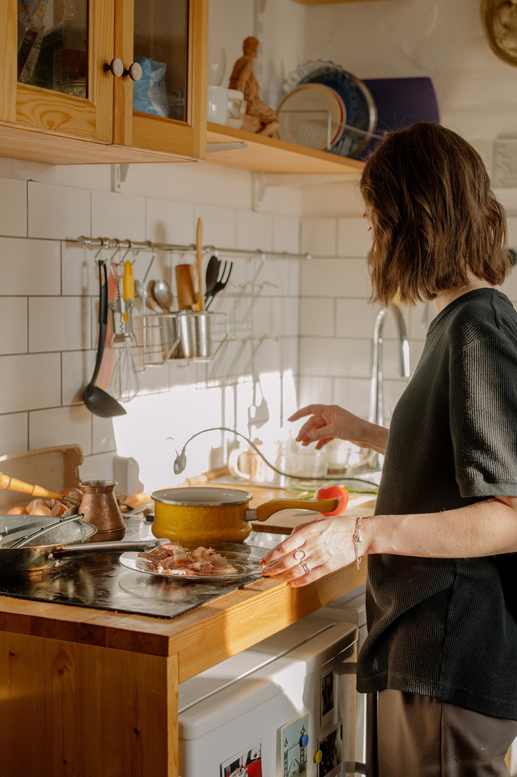 Woman in grey T-shirt, standing in front of kitchen sink, cooking on a ceramic hob countertop kitchen. Photo by CottonBro Studio on Pexels.