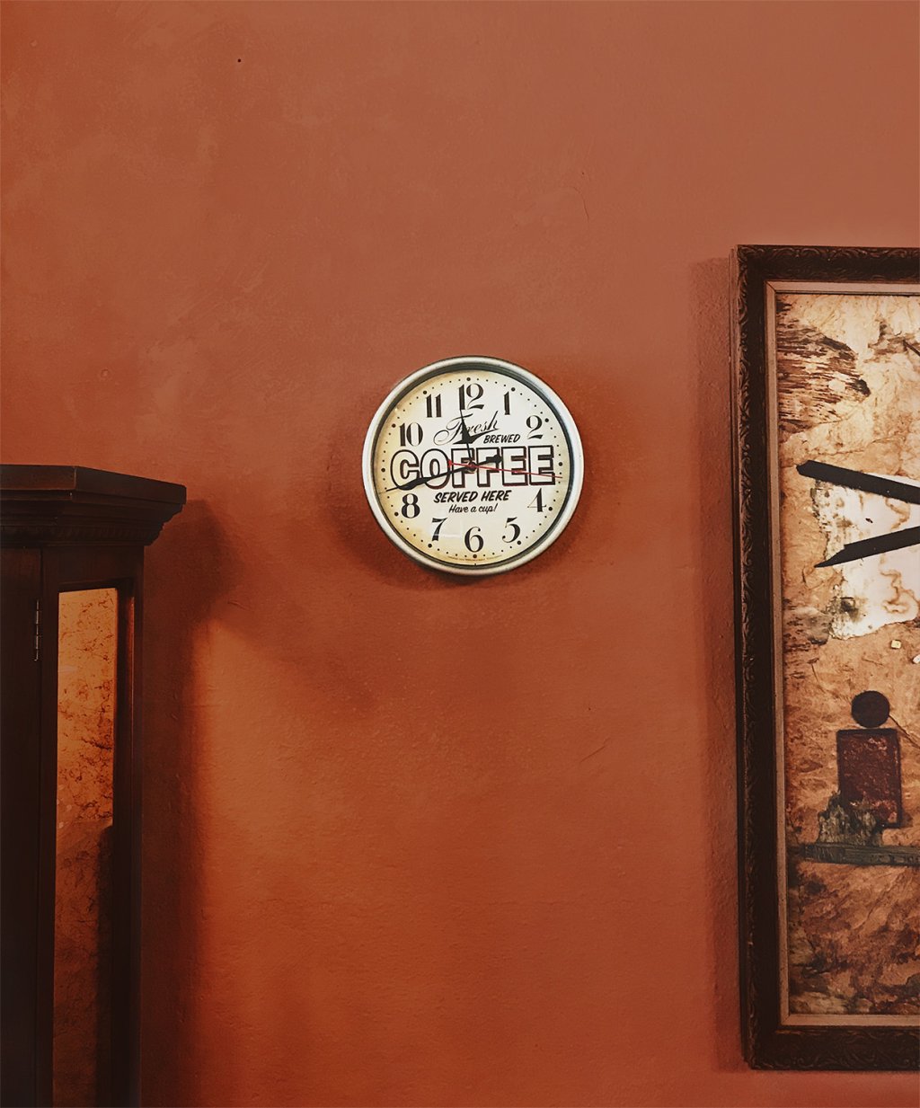 Kitchen or dining room with earthy red wall, clock on the wall and painting hanging.